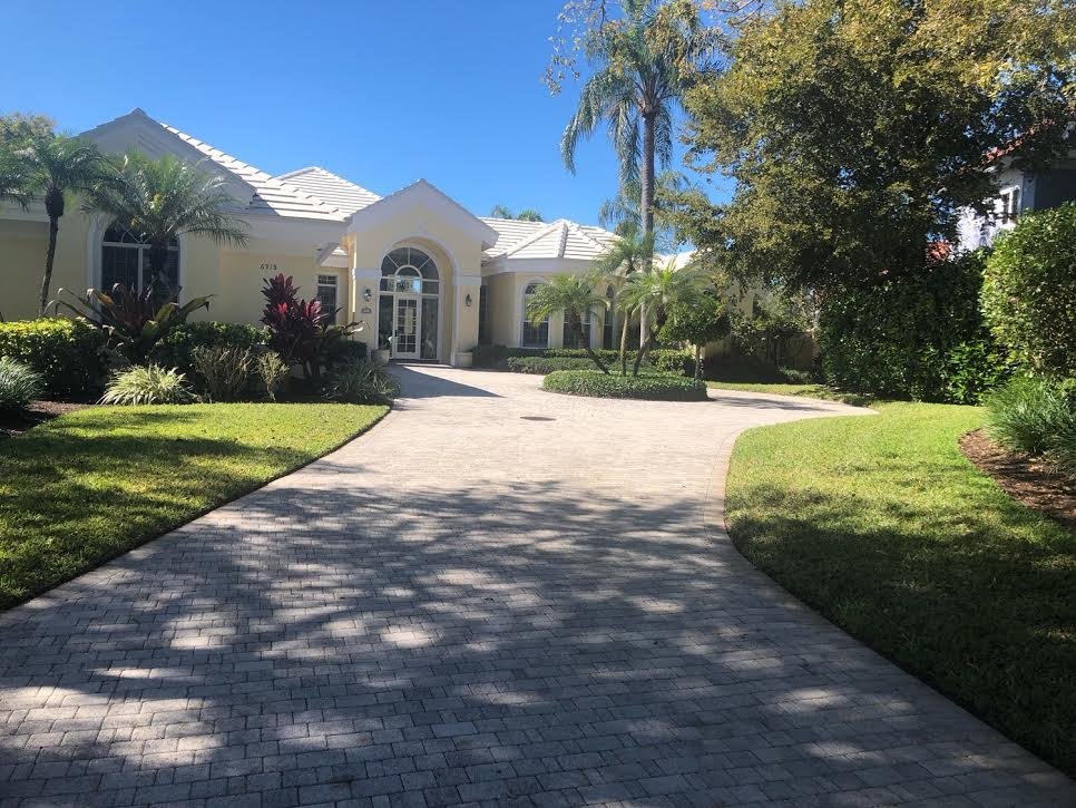 Manicured lawn and beds along a paver driveway at a Naples home